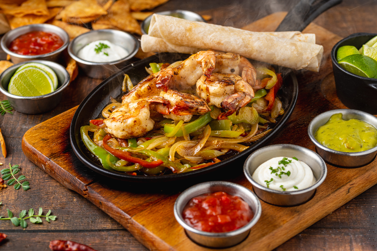 Shrimp fajitas on wooden table with sauces and tortillas on the side