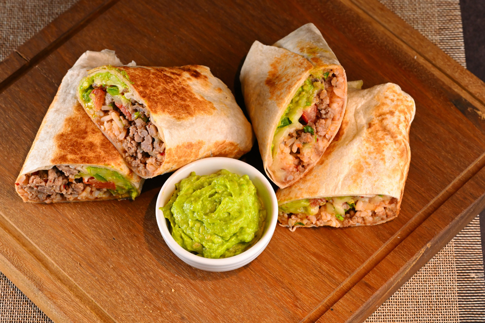 Healthy Mexican meal, sliced meat burrito with guacamole on a white bowl