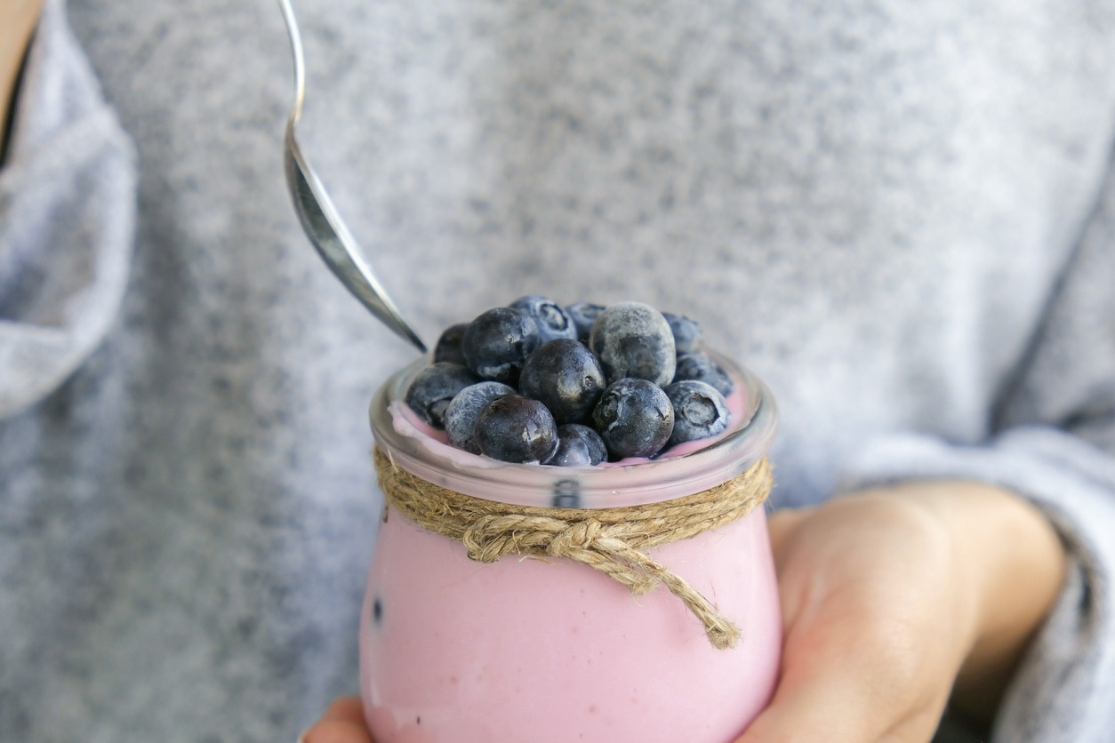 Female-hands-holding-Bowl-with-yogurt-and-blueberries-on-table