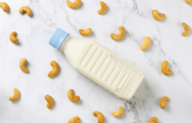 Image-of-a-bottle-of-cashew-milk-and-cashews-spread-across-in-the-white-background