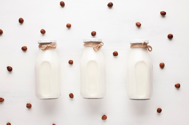Image-of-three-milk-bottles-and-hazelnuts-spread-across-in-the-white-background