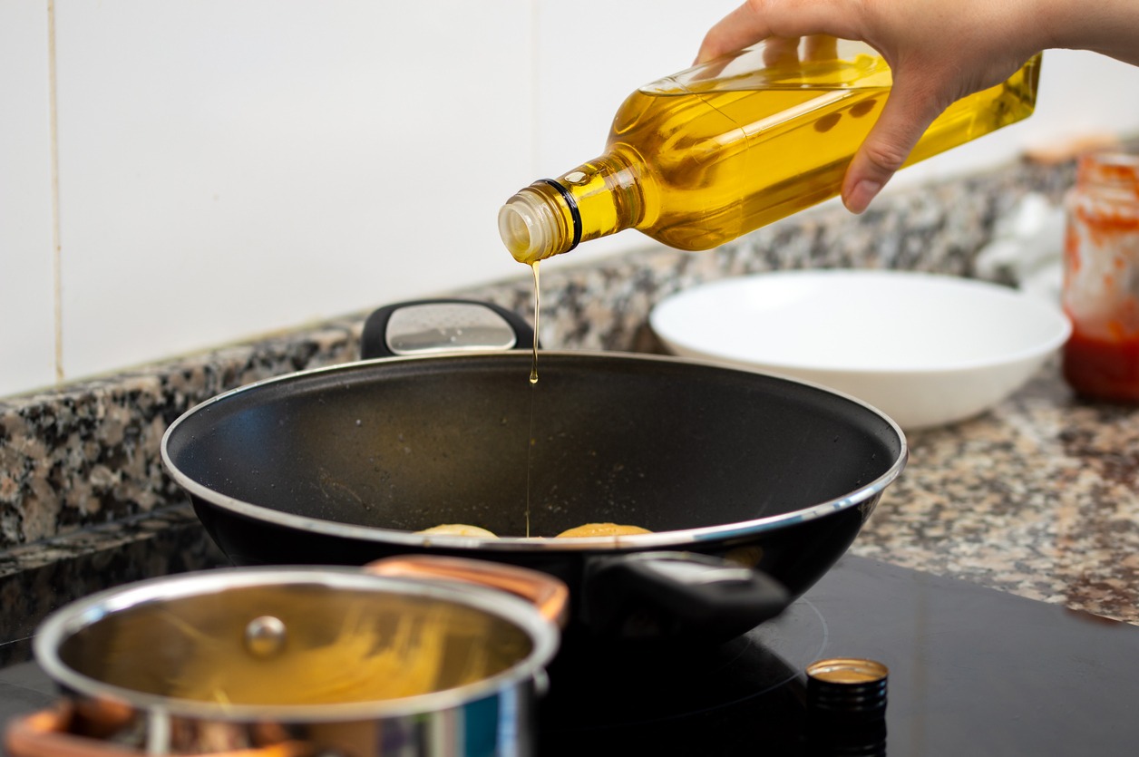 Woman-pouring-cooking-oil-from-bottle-into-frying-pan