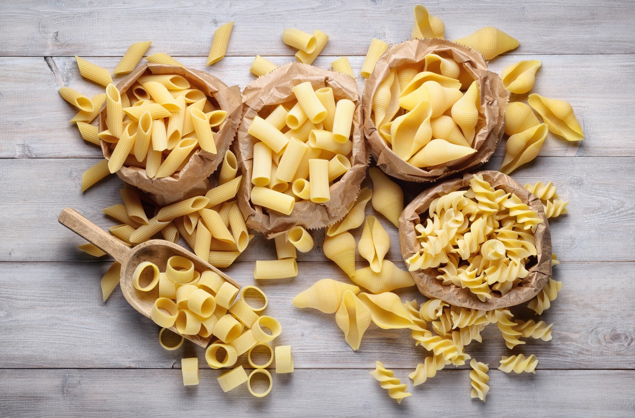 Assortment of raw pasta: pens, shells, rigatoni, fusilli and squid on wooden background, top view